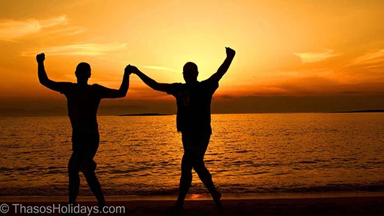 Two people greek dancing on a beach during sunset